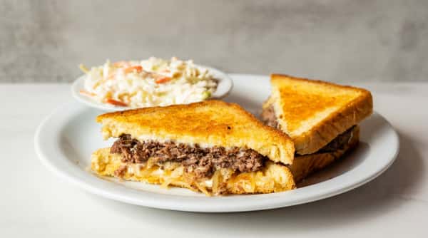 Grilled patty melt sandwich filled with beef and melted cheese, served with creamy coleslaw on a white plate.