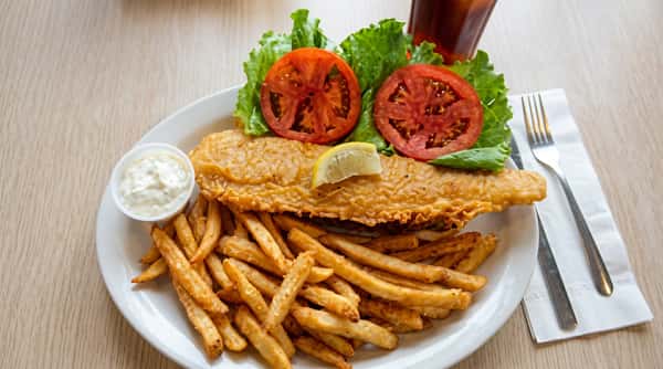 Golden breaded fish fillet served with seasoned French fries, tartar sauce, lemon wedges, fresh lettuce, and sliced tomatoes.