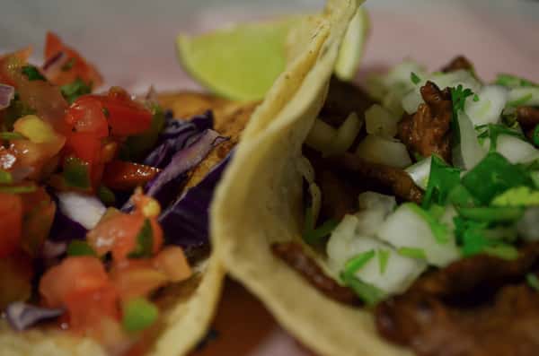 Closeup of two different tacos with a lime wedge in the background.