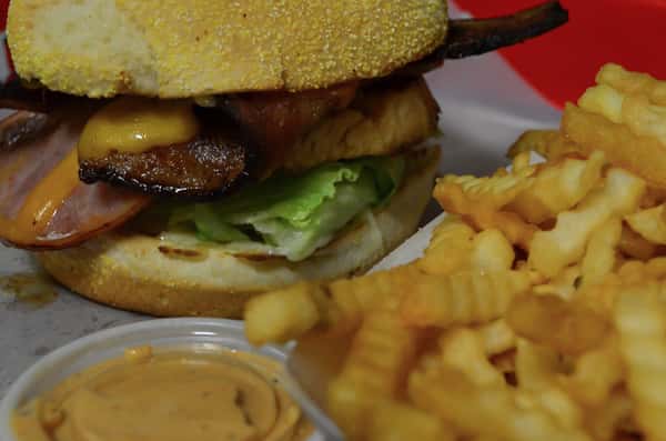 Closeup of the Chicken Club. Grilled chicken breast topped with bacon, ham, Swiss cheese, lettuce, tomato, and mayo. Served with a side of french fries.