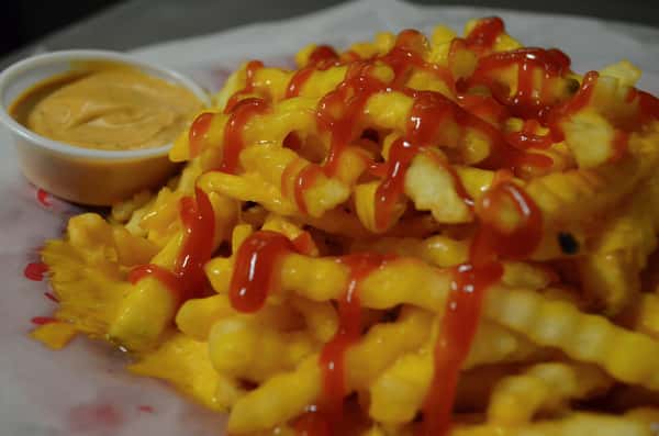 French fries covered with ketchup and a side of dipping sauce.