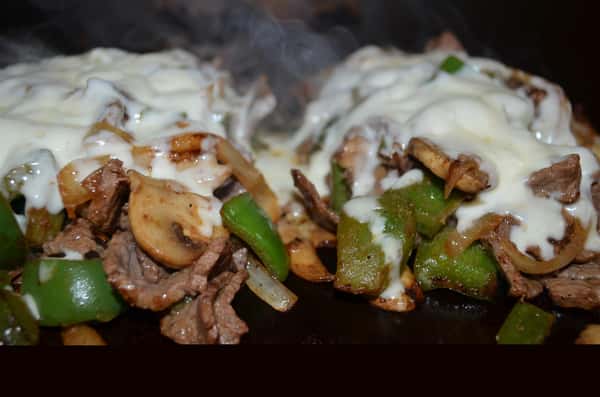 Steak, mushroom, onions and green onions all being cooked on a grill.