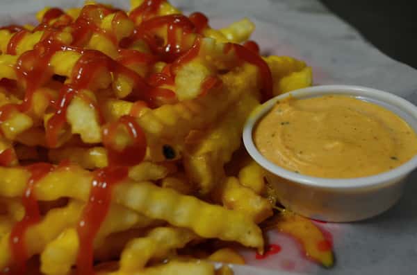 French fries covered with ketchup and a side of dipping sauce.