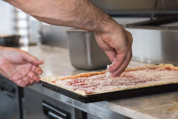 chef putting cheese on a flat pizza