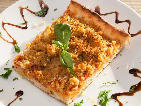 slice of pizza with bread crumbs and basil leaves