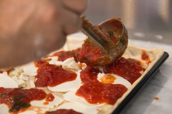 chef putting sauce on a flat pizza