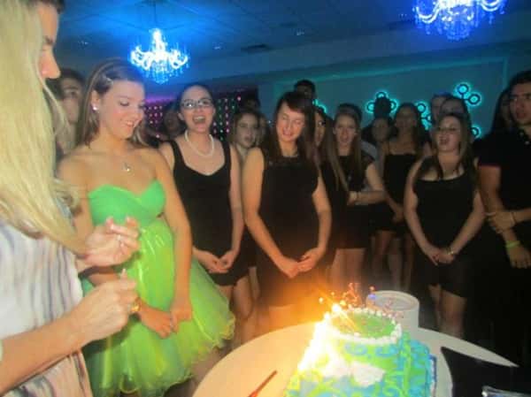 people standing around lit birthday cake singing happy birthday