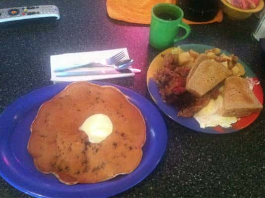 Pancake with butter on plate and eggs with toast and bacon on plate