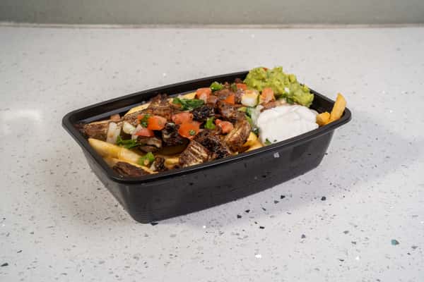 Beef fajita asada fries topped with grilled meat, vegetables, guacamole, and sour cream in a black tray.