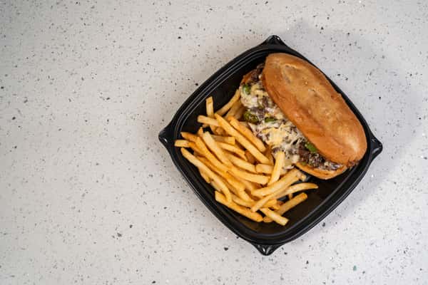Philly cheesesteak sandwich served with french fries in a black takeout tray.