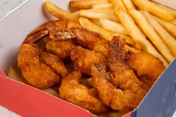 Close-up of Cajun shrimp served with french fries in a takeout box.