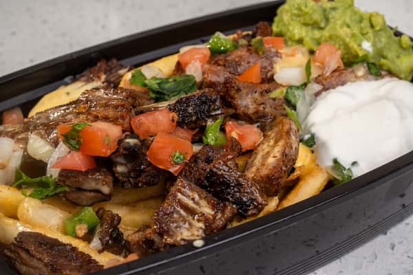 Close-up of beef fajita asada fries topped with grilled meat, pico de gallo, guacamole, and sour cream.