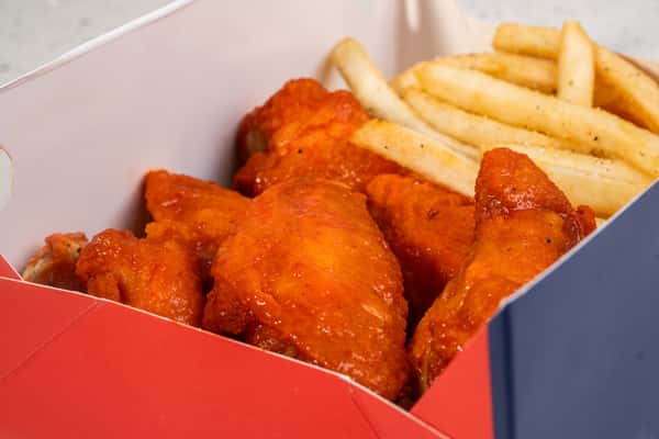 Close-up of buffalo wings served with french fries in a takeout box.