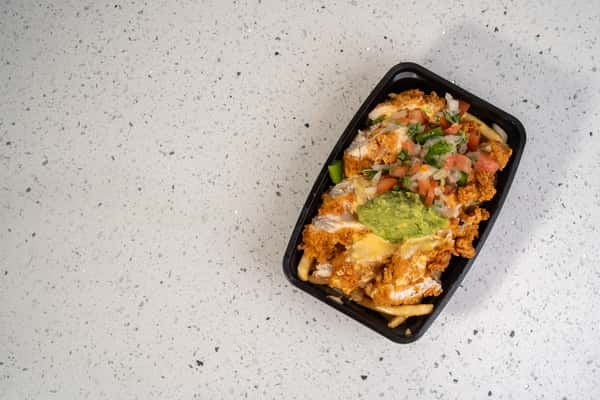 Overhead view of loaded fries topped with meat, cheese, vegetables, and guacamole.