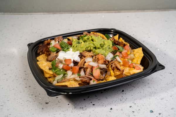 Loaded nachos topped with meat, cheese, vegetables, sour cream, and guacamole.