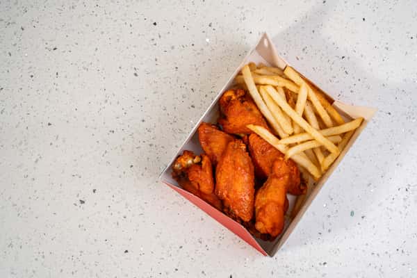Overhead view of buffalo wings served with french fries in a takeout box.