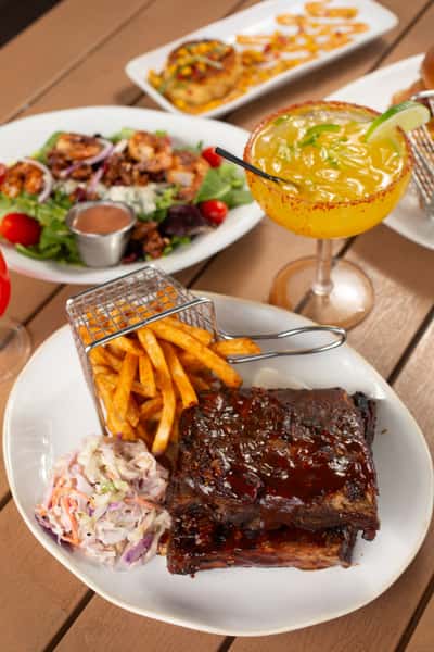 Barbecue baby back ribs with seasoned fries, coleslaw, and frozen mango margarita served at a tropical waterfront restaurant