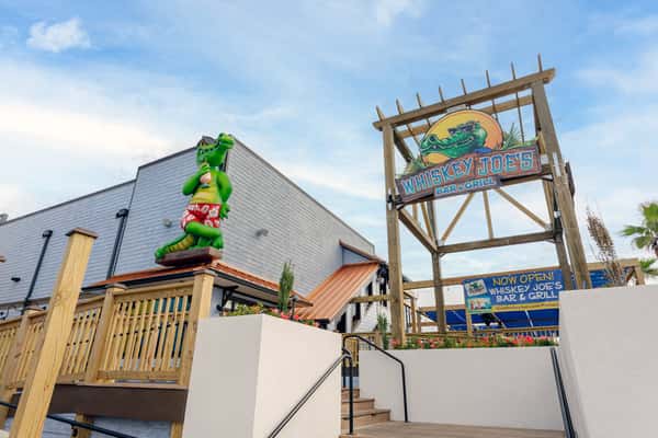 Exterior entrance of Whiskey Joe's Bar & Grill featuring the signature alligator sign and tropical waterfront restaurant atmosphere