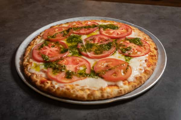 Pizza with sliced tomatoes and a drizzle of pesto