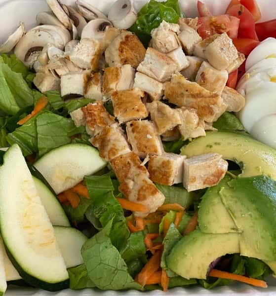 A salad topped with avocado, cucumber, tomato, hard boiled egg, mushroom, and grilled chicken