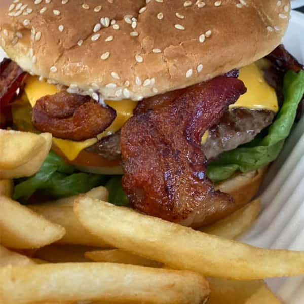 A cheeseburger topped with bacon and lettuce with a side of french fries