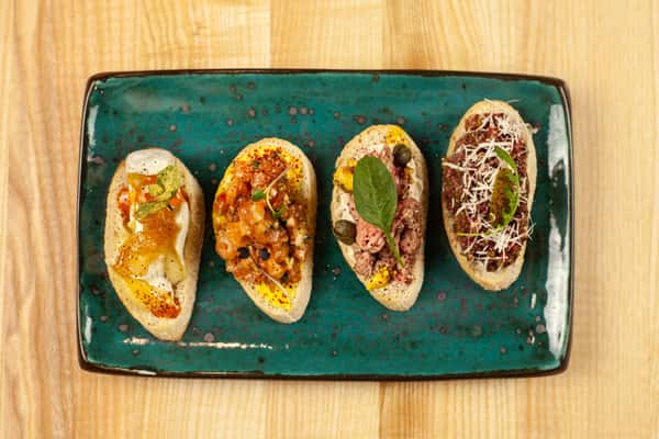 Delicious bruschetta assortment with diverse toppings on a teal plate.