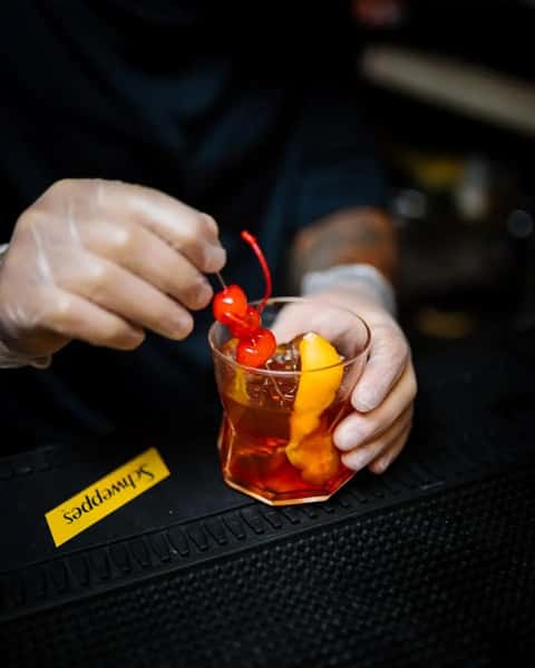 bartender garnishing a cocktail with cherry and fruit in a dimly lit bar setting