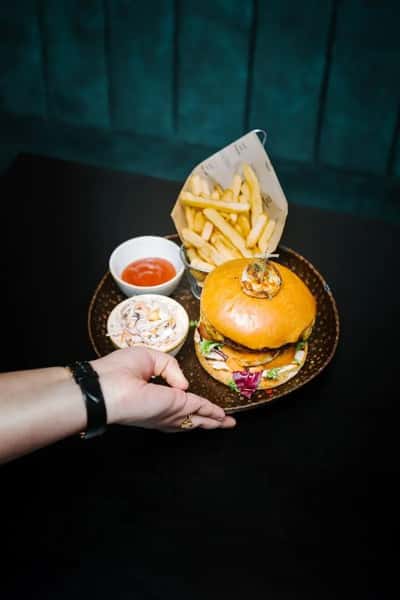 Juicy gourmet burger with melted cheese served with crispy fries, dipping sauces, and slaw on a restaurant table