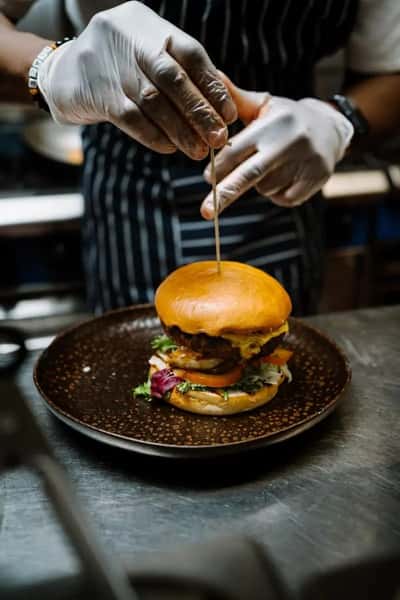 chef assembling a stacked burger with fresh toppings in a restaurant kitchen