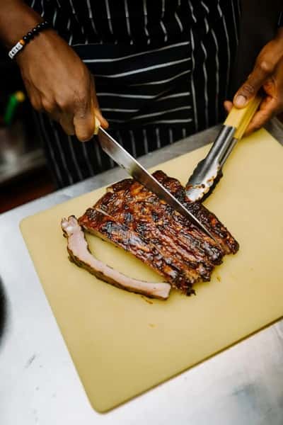 barbecue ribs being sliced on a cutting board with a chef's knife in a kitchen setting