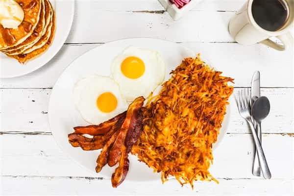 Hash browns with a side of bacon and two sunny side up eggs on a plate