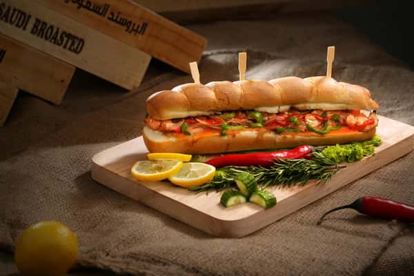 A long sandwich with skewers, alongside lemon slices, chili peppers, and cucumber on a wooden board at Pierce Creek.
