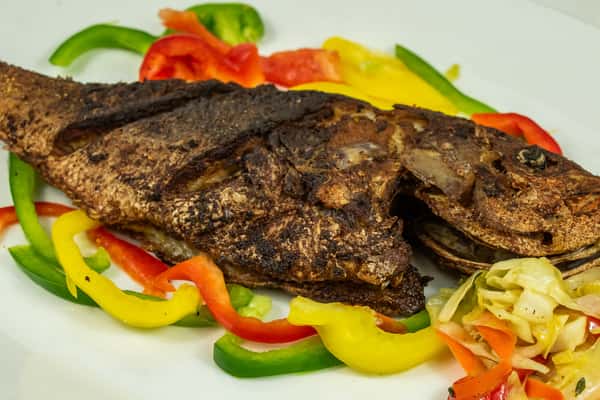 Whole seasoned and grilled fish served with colorful bell pepper strips and sautéed cabbage on a white plate.
