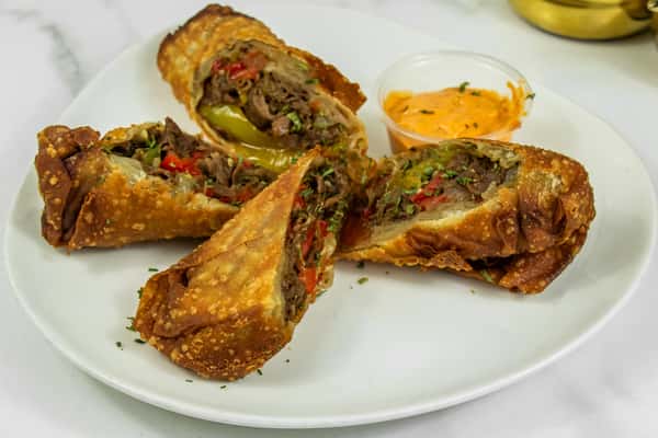 Golden fried Philly cheesesteak egg rolls stuffed with beef, peppers, and onions, served with a side of spicy dipping sauce.