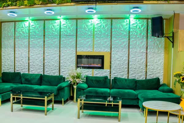 Chic lounge area with emerald green velvet sofas, glass-top tables, a modern electric fireplace, and ambient green lighting.