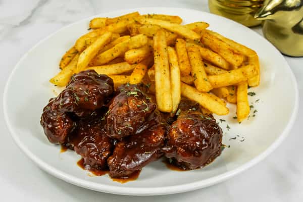 Barbecue-glazed chicken wings served with seasoned French fries on a white plate.