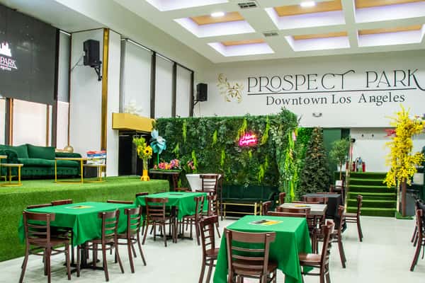Vibrant event space at Prospect Park Downtown Los Angeles with green-themed decor, stage seating, and floral wall featuring neon sign.