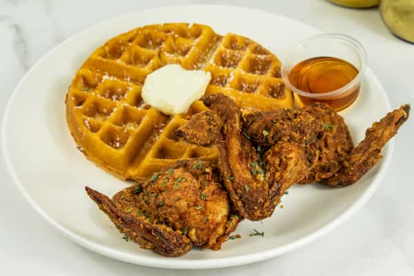 Crispy fried chicken wings served with a golden waffle, topped with butter and a side of syrup.