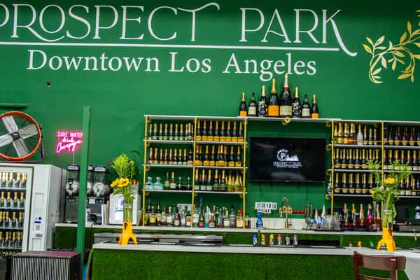 Green-themed bar at Prospect Park Downtown Los Angeles, with champagne bottle displays and a vibrant, modern atmosphere.