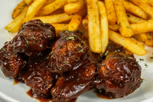 Barbecue-glazed chicken wings served with seasoned French fries on a white plate.
