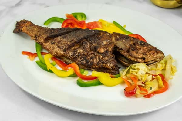 Whole seasoned and grilled fish served with colorful bell pepper strips and sautéed cabbage on a white plate.