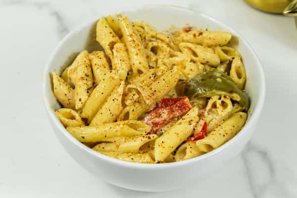 Creamy penne pasta with bell peppers and spices served in a white bowl on a marble surface.