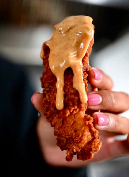 Hand holding a chicken tender dripping with sauce