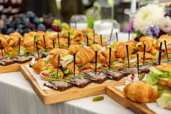 Gourmet catering spread featuring mini croissant sandwiches and open-faced canapés on wooden boards, ideal for upscale brunch or private event catering.