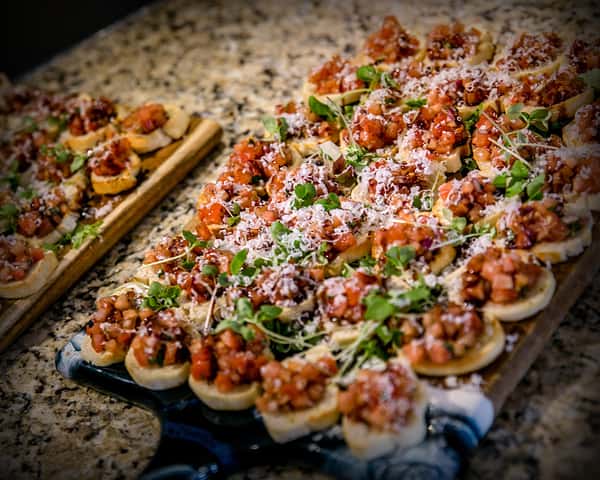 Artisan crostini platter topped with diced tomatoes, herbs, and shaved cheese, presented as a rustic Italian-inspired appetizer for catered events.