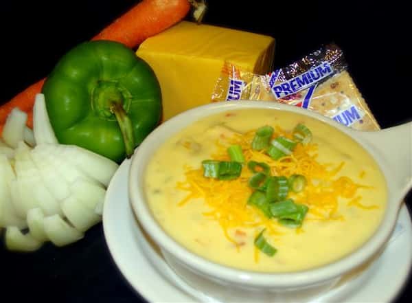 Soup with side of saltines and peppers and onions in the background