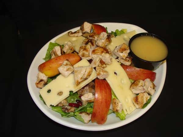 Salad topped with swiss cheese apples walnuts cranberries and sauce