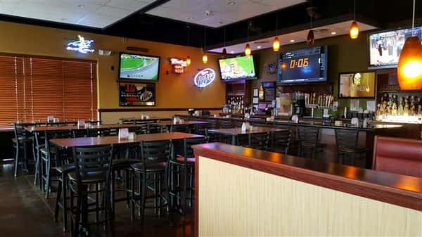 interior of restaurant with televisions on the wall and brown tables with black chairs