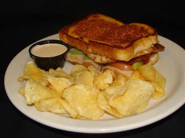 Grilled sandwich with side of potato chips and sauce