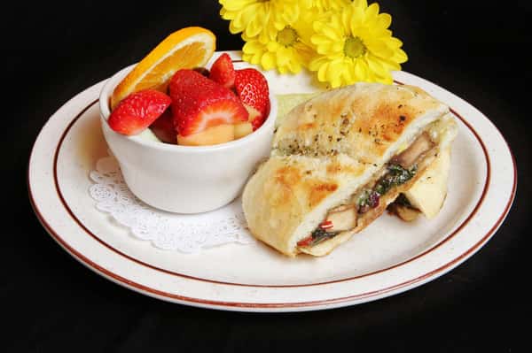 Grilled chicken panini with a bowl of sliced strawberries and oranges